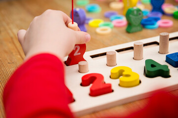 Child playing with different color wooden rings. Sequence, fine motor skills, therapy task for education and brain exercise. Counting math play game. Montessori type implement. Wooden toys.