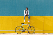 Man With Smart Phone And Bicycle Sitting On Yellow Wall