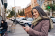 © ADDICTIVE STOCK - Smiling woman with coffee cup using smartphone on street