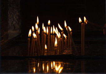 Sticker - A closeup shot of some candles burning in the dark in a church