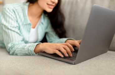 Wall Mural - Cropped view of Indian woman using laptop while lying on couch at home