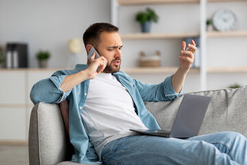 Poster - Stressed young businessman using laptop and making call on mobile phone from home office