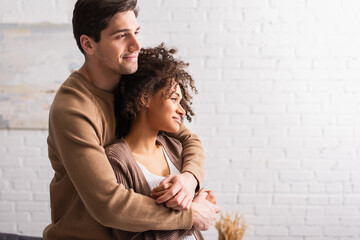 Smiling man hugging curly african american girlfriend at home