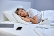 © Roman - woman laying in pajamas on bed in bedroom. Bright white interior. european european female fell asleep with smartphone next to her. In the morning on holidays. leisure, resting, relax, dreams