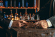 © TSViPhoto - Man's hands with brandy glass on the bar counter. Alcoholic beverage, cognac, whiskey, port, brandy, rum, scotch, bourbon. Vintage wooden table in the dark