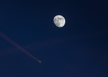 Closeup Of The Waxing Moon And An Airplane Passing Close By, Leaving A Contrail Which Is Illuminated By The Setting Sun - Evening Capture Against Dark Blue Sky. Stuttgart, Germany January 22, 2022