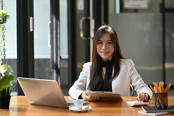 Wall Mural - Successful business woman sitting in office and smiling to camera.