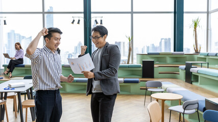 Two young male startup owners reach a solution for business plan. Two young co-workers give high five when they both set mutual solution to solve any issue in a green co-working office