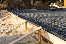 Iron fittings on a wooden formwork with laid pipes are the basis for pouring the foundation of the house with a concrete slab. Construction of cottages, design, engineering communications.