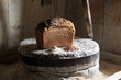 Bread from whole grain flour from the oven, lies on stone millstones in a wooden house, next to wheat grains and flour. Food.