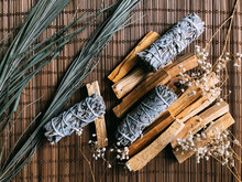 Incense On A Bamboo Brown Stand Close-up, Palo Santo From Peru And California White Sage, Dried Flowers Around. Art Background For Text With Natural Incense And Light Background Blur