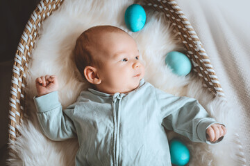 Cute baby Easter bunny. Little baby boy with bunny ears and Easter eggs in wicker basket in white fur. Symbol of Easter holiday, birth, spring, religion.