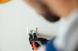 © Kostiantyn - Close up of hands of male worker, professional electrician in protective gloves using screwdriver while installing new electrical socket outlet in a room