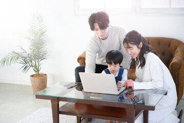 メインビジュアルにも使える家族でパソコンを使うリビングでの様子　コピースペースあり　やや俯瞰