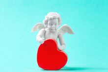 Angel Baby And Red Heart On Blue Background. Cute Valentines Day Greeting With Little Cherub Figurine