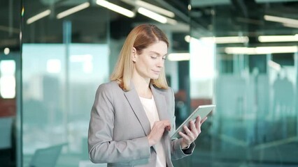 business woman use digital tablet while standing in modern office. Indoor. Female office worker looking at smartphone screen. Confident blonde businesswoman accountant or broker, office worker Browse