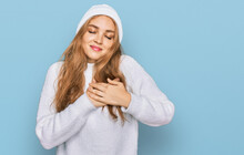 Young Caucasian Girl Wearing Wool Sweater And Winter Cap Smiling With Hands On Chest With Closed Eyes And Grateful Gesture On Face. Health Concept.