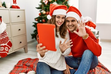 Wall Mural - Young hispanic couple wearing christmas hat having video call using touchpad at home.