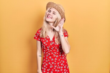 Poster - Beautiful caucasian woman with blond hair wearing summer hat smiling with hand over ear listening an hearing to rumor or gossip. deafness concept.