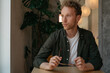© Oleksii - Portrait of young pensive man holding eyeglasses planning project looking at window sitting in cafe