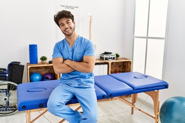 Canvas Print - Young hispanic man wearing physio therapist uniform with arms crossed gesture at clinic