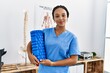 Young african american woman wearing physio therapist uniform holding foam roller at clinic