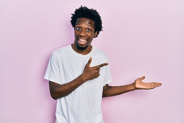 Sticker - Young african american man wearing casual white t shirt amazed and smiling to the camera while presenting with hand and pointing with finger.