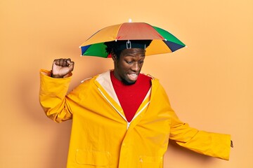 Poster - Young african american man wearing yellow raincoat dancing happy and cheerful, smiling moving casual and confident listening to music