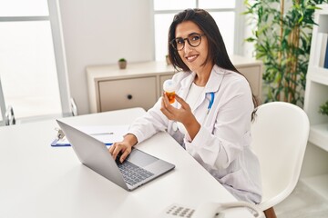 Wall Mural - Young hispanic woman wearing doctor uniform holding pills working at clinic