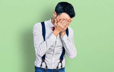 Poster - Hispanic man with beard wearing hipster look with bow tie and suspenders with sad expression covering face with hands while crying. depression concept.