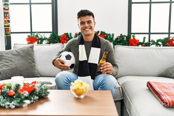 Sticker - Young hispanic man football hooligan holding ball and beer looking positive and happy standing and smiling with a confident smile showing teeth