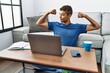 © Krakenimages.com - Young handsome hispanic man using laptop sitting on the floor showing arms muscles smiling proud. fitness concept.