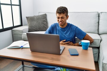 Sticker - Young handsome hispanic man using laptop sitting on the floor with hand on stomach because nausea, painful disease feeling unwell. ache concept.