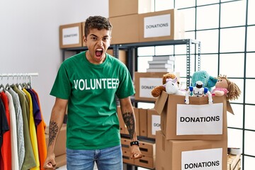 Canvas Print - Young handsome hispanic man wearing volunteer t shirt at donations stand angry and mad screaming frustrated and furious, shouting with anger. rage and aggressive concept.