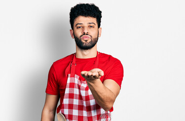 Poster - Young arab man with beard wearing cook apron looking at the camera blowing a kiss with hand on air being lovely and sexy. love expression.