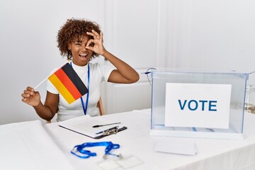 Sticker - Young african american woman at political campaign election holding germany flag smiling happy doing ok sign with hand on eye looking through fingers