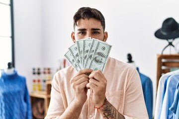 Sticker - Young hispanic man holding dollars banknotes at retail shop relaxed with serious expression on face. simple and natural looking at the camera.