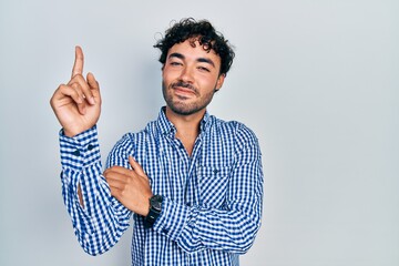 Sticker - Young hispanic man wearing casual clothes with a big smile on face, pointing with hand and finger to the side looking at the camera.