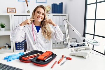 Poster - Young beautiful doctor woman with reflex hammer and medical instruments smiling cheerful showing and pointing with fingers teeth and mouth. dental health concept.