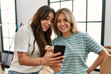 Young beautiful couple smiling happy using smartphone at new home.