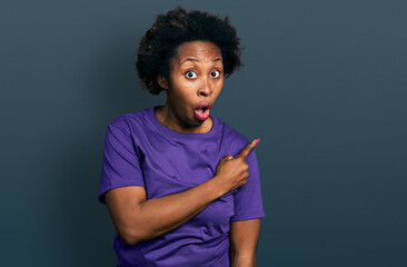 Sticker - African american woman with afro hair wearing casual purple t shirt surprised pointing with finger to the side, open mouth amazed expression.