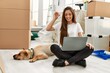 © Krakenimages.com - Young hispanic woman holding key having video call sitting on floor with dog at new home