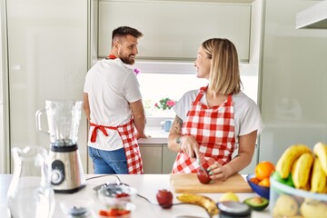 Wall Mural - Young couple smiling confident making smoothie cooking at kitchen