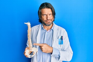 Wall Mural - Middle age handsome traumatologist man holding anatomical model of spinal column skeptic and nervous, frowning upset because of problem. negative person.