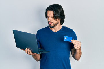 Canvas Print - Middle age caucasian man wearing business style holding laptop and credit card skeptic and nervous, frowning upset because of problem. negative person.