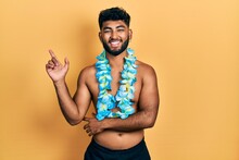 Arab Man With Beard Wearing Swimsuit And Hawaiian Lei Smiling Happy Pointing With Hand And Finger To The Side