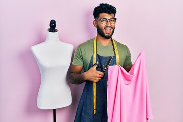 Wall Mural - Arab man with beard dressmaker designer holding scissors and cloth celebrating crazy and amazed for success with open eyes screaming excited.