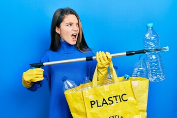 Sticker - Young brunette girl holding recycling bag with plastic bottles and waste picker angry and mad screaming frustrated and furious, shouting with anger. rage and aggressive concept.