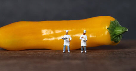 Two miniature chefs standing in front of yellow paprika. The concept of miniature people and fresh ingredients.
