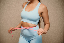Cropped View Of Slim Woman Measuring Waist With Tape Measure At Home, Close Up. Unrecognizable European Woman Checking The Result Of Diet For Weight Loss Or Liposuction Indoors